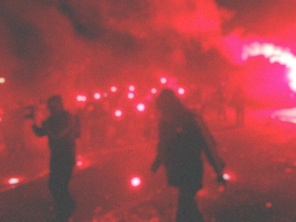 Ein verschwommenes Bild, rotes Feuerwerk und Rauch, schemenhafte Personen